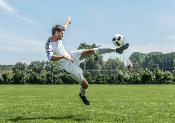 Cầu thủ bóng đá nhảy để đá bóng trên sân